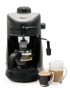Front facing view of 4 cup espresso machine in black with silver panel on the lid featuring glass carafe. An espresso and cappuccino sit to the right of the machine.